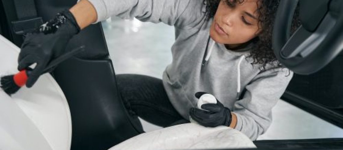 Service station worker brushing out ingrained dirt from vehicle upholstery