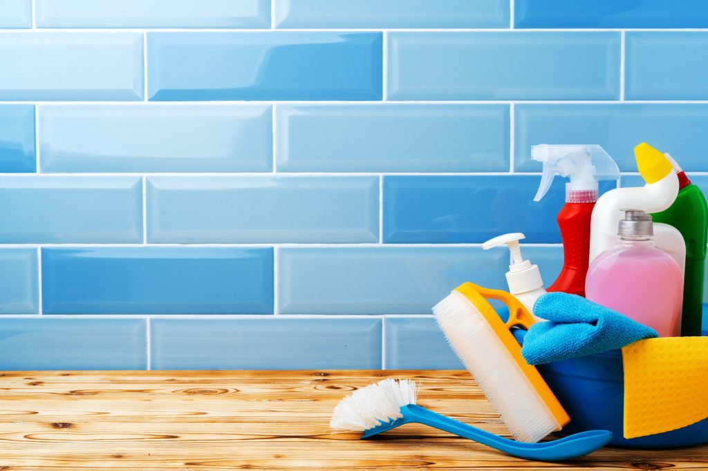 Household detergents and cleaning tools against blue tile background